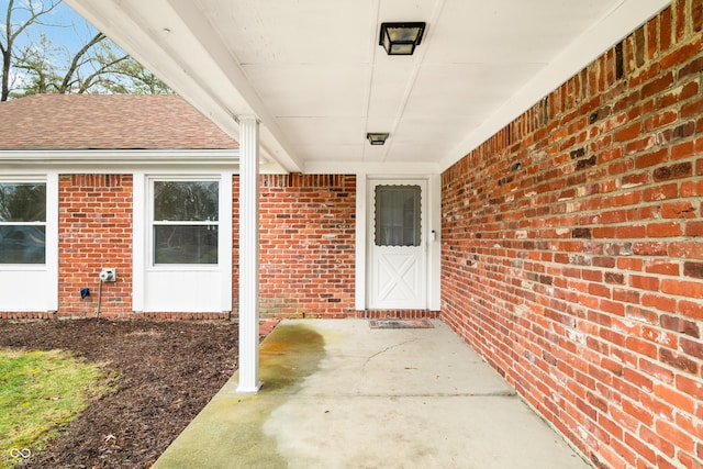 entrance to property with brick siding and a shingled roof