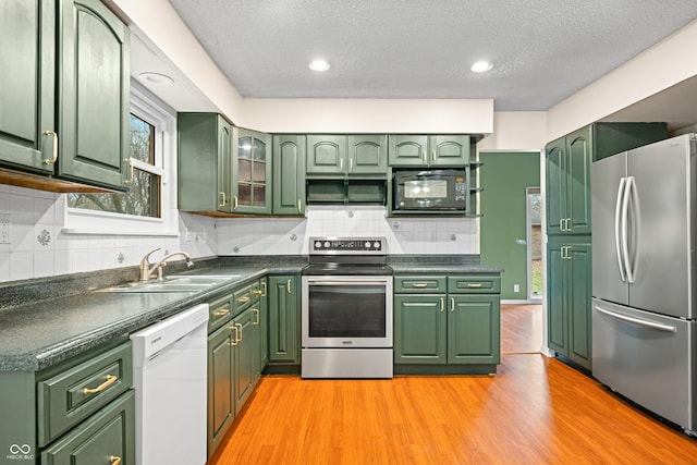 kitchen featuring stainless steel appliances, light wood finished floors, a sink, and green cabinetry