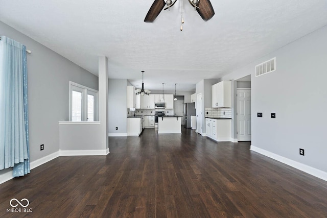 unfurnished living room with ceiling fan with notable chandelier, a textured ceiling, and dark hardwood / wood-style floors