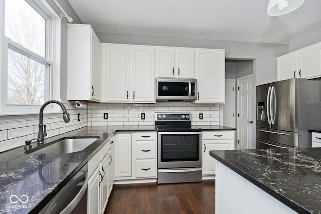 kitchen with stainless steel appliances, white cabinets, dark stone counters, and sink