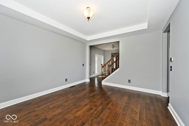 empty room with dark hardwood / wood-style floors and a raised ceiling