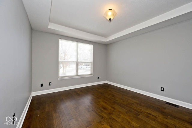 spare room featuring a tray ceiling and dark hardwood / wood-style floors