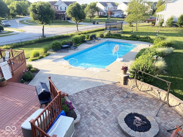 view of pool with a patio area, a wooden deck, an outdoor fire pit, a yard, and a trampoline