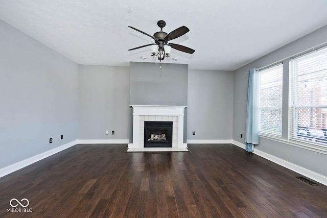 unfurnished living room with dark wood-type flooring, a tiled fireplace, and ceiling fan