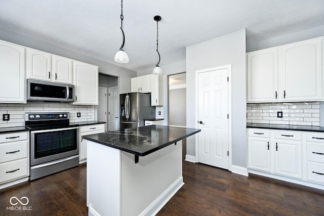 kitchen with white cabinets, appliances with stainless steel finishes, a kitchen island, decorative light fixtures, and dark wood-type flooring