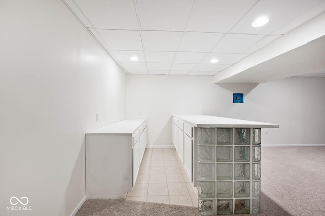 interior space featuring light carpet, white cabinets, and a paneled ceiling