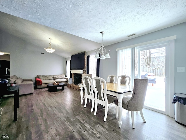 dining room with a fireplace, a textured ceiling, vaulted ceiling, a chandelier, and hardwood / wood-style floors