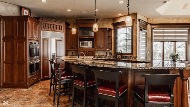 kitchen featuring a kitchen bar, hanging light fixtures, dark stone counters, and built in appliances