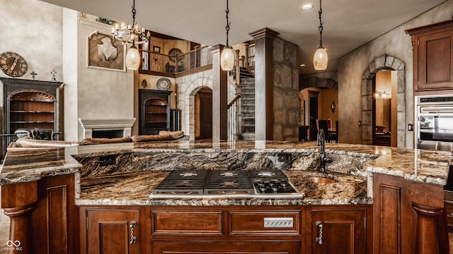 kitchen with pendant lighting, appliances with stainless steel finishes, dark stone counters, sink, and a notable chandelier