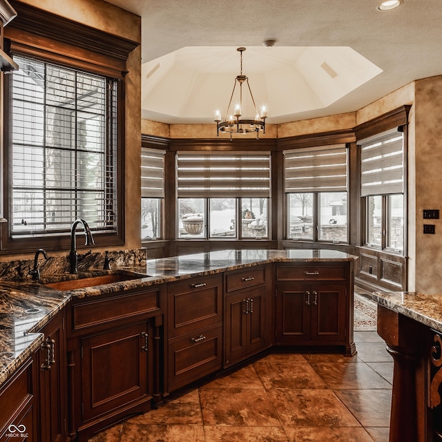 kitchen featuring pendant lighting, a wealth of natural light, sink, an inviting chandelier, and dark stone counters