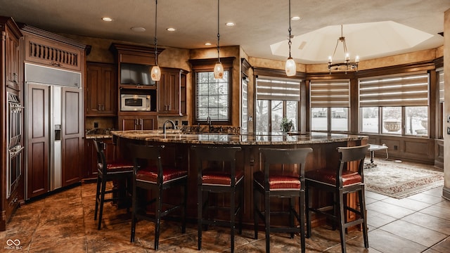 bar featuring stone countertops, hanging light fixtures, built in appliances, and an inviting chandelier