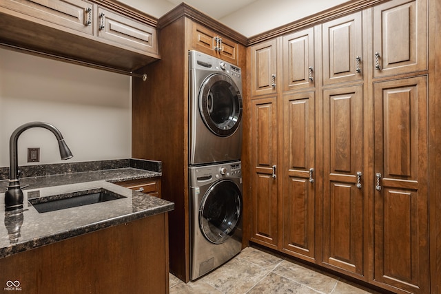 clothes washing area with stacked washer / drying machine, sink, and cabinets