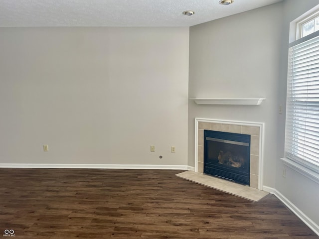 unfurnished living room with a tile fireplace, dark wood-type flooring, and a textured ceiling