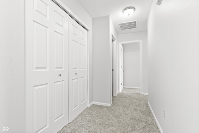 hallway featuring light colored carpet, visible vents, and baseboards