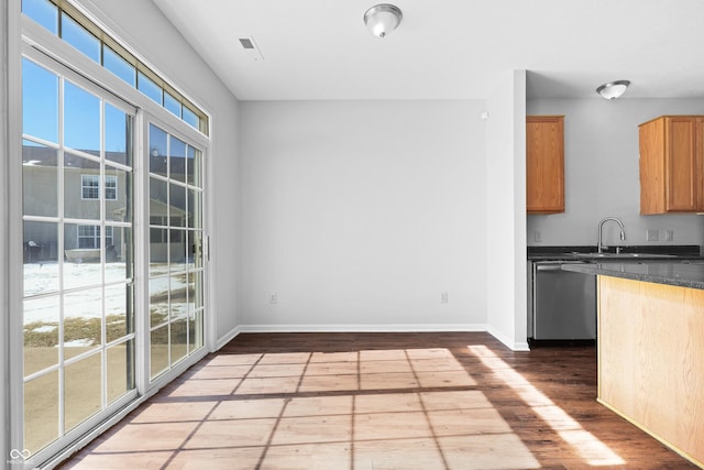 kitchen featuring wood finished floors, baseboards, stainless steel dishwasher, dark countertops, and plenty of natural light