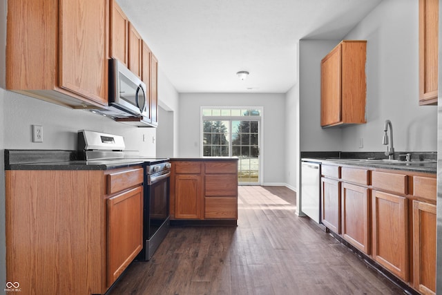 kitchen featuring baseboards, dark countertops, appliances with stainless steel finishes, dark wood-type flooring, and a sink