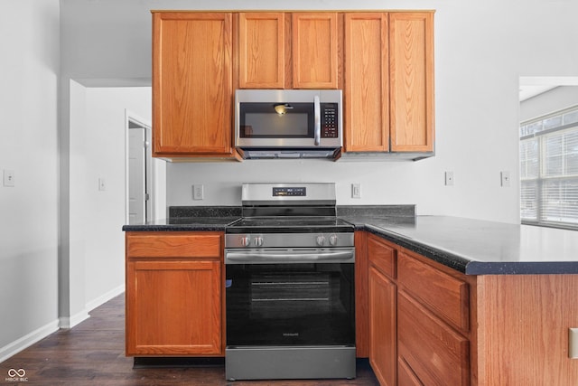 kitchen featuring baseboards, dark countertops, appliances with stainless steel finishes, dark wood-style flooring, and a peninsula