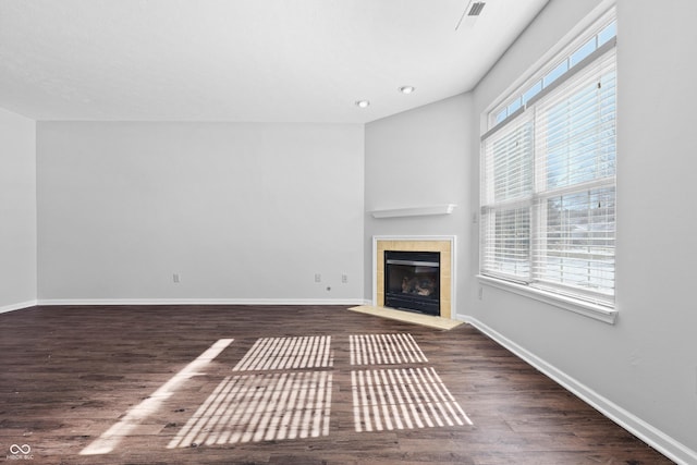 unfurnished living room with dark wood-style floors, baseboards, a wealth of natural light, and a tile fireplace