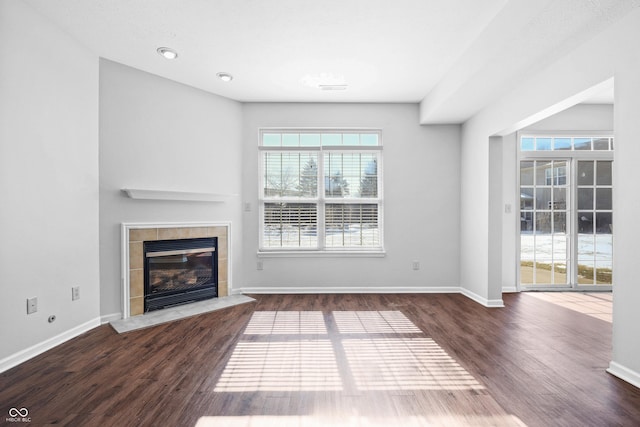 unfurnished living room featuring a tile fireplace, dark wood finished floors, visible vents, and baseboards