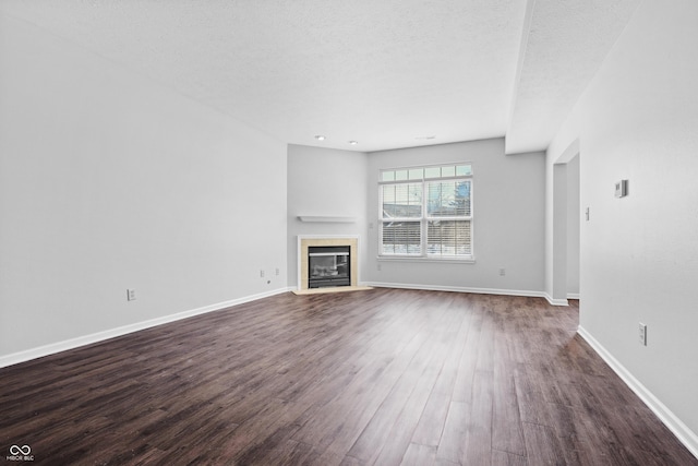 unfurnished living room featuring a textured ceiling, a tiled fireplace, baseboards, and dark wood-style flooring