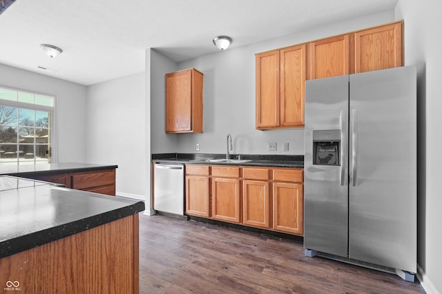 kitchen featuring dark countertops, dark wood-style floors, stainless steel appliances, and a sink