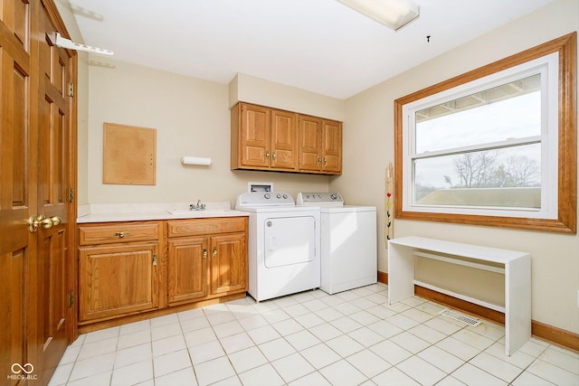 laundry area with sink, light tile patterned floors, washing machine and dryer, and cabinets