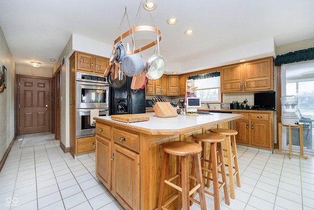 kitchen with a breakfast bar, light tile patterned floors, double oven, an island with sink, and backsplash