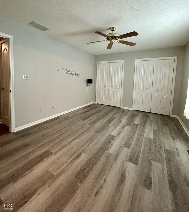 unfurnished bedroom featuring multiple closets, ceiling fan, a textured ceiling, and hardwood / wood-style flooring