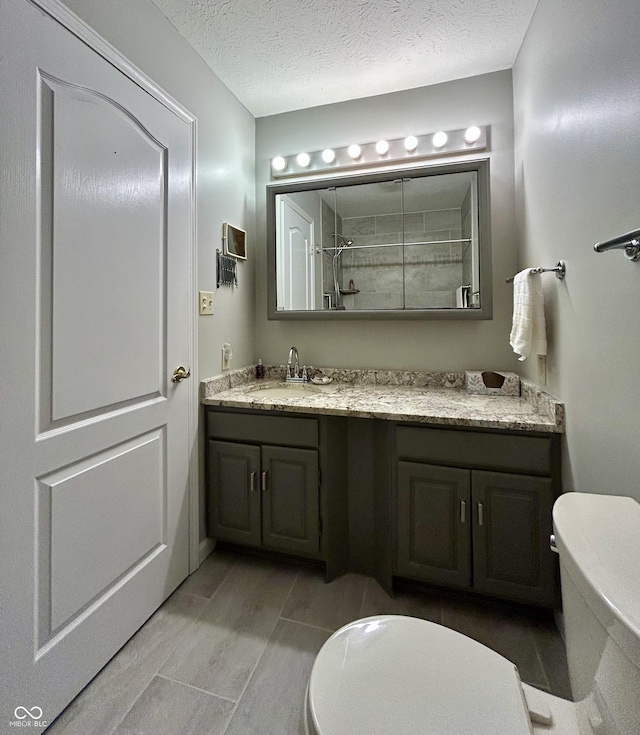 bathroom with a shower, vanity, a textured ceiling, and toilet