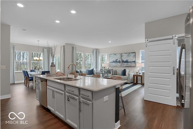 kitchen with a barn door, stainless steel appliances, a sink, dark wood finished floors, and a center island with sink