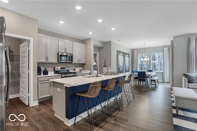 kitchen with a kitchen island with sink, stainless steel appliances, dark wood-type flooring, a kitchen breakfast bar, and light countertops