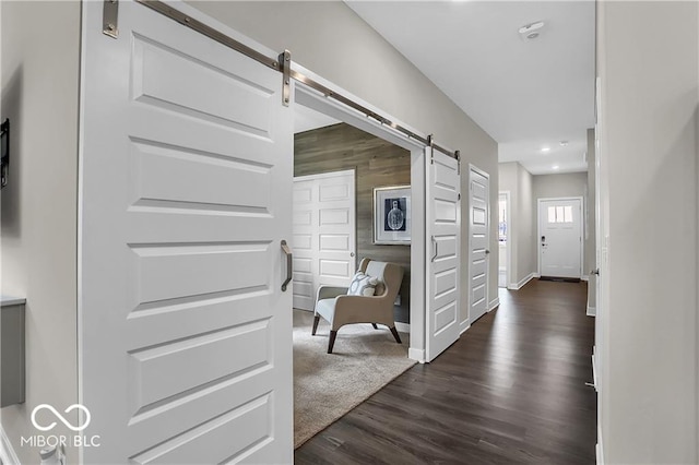 hallway with dark wood-type flooring, baseboards, and a barn door