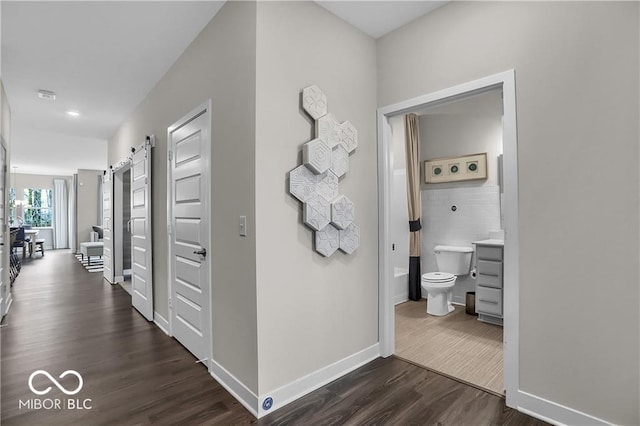 corridor featuring a barn door, dark wood-style flooring, tile walls, and baseboards