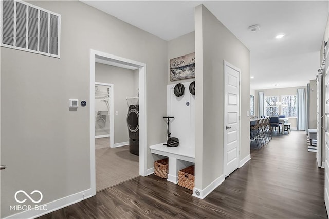 hallway featuring dark wood-type flooring, visible vents, baseboards, washer / clothes dryer, and an inviting chandelier