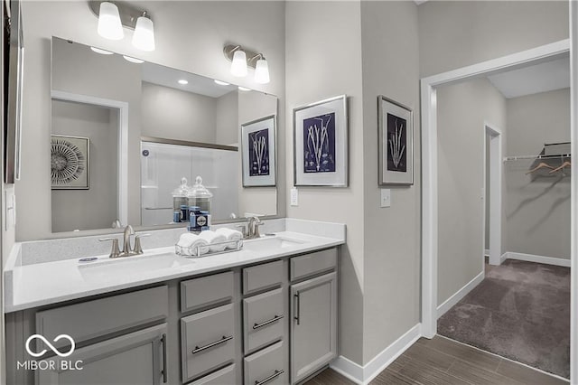 full bathroom featuring a walk in closet, a sink, baseboards, and double vanity