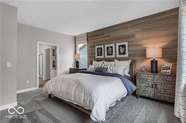 bedroom featuring wooden walls, baseboards, ensuite bath, an accent wall, and carpet floors