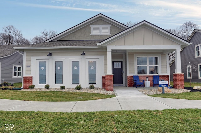 view of front of house featuring brick siding, roof with shingles, a porch, board and batten siding, and a front yard