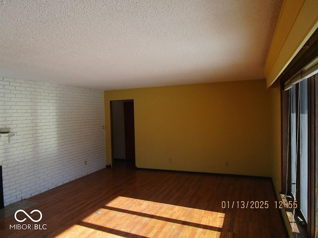 empty room featuring brick wall, a textured ceiling, baseboards, and wood finished floors