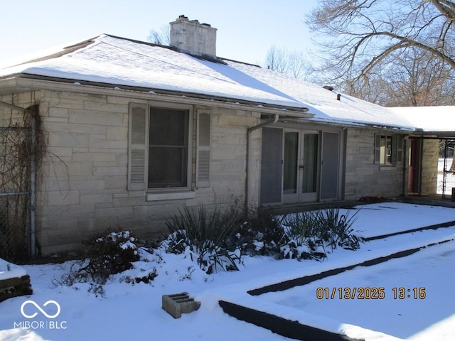 view of snow covered exterior with stone siding, french doors, and a chimney