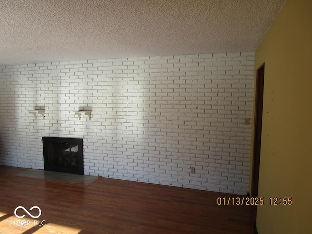 unfurnished living room featuring a large fireplace, brick wall, a textured ceiling, and wood finished floors