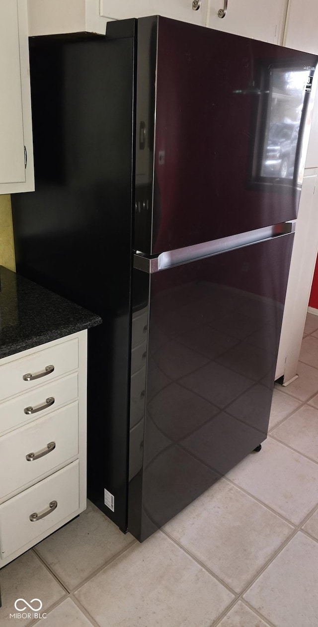 kitchen with light tile patterned flooring, freestanding refrigerator, and white cabinetry