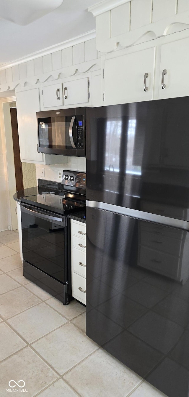 kitchen featuring dark countertops, freestanding refrigerator, white cabinetry, light tile patterned flooring, and black / electric stove