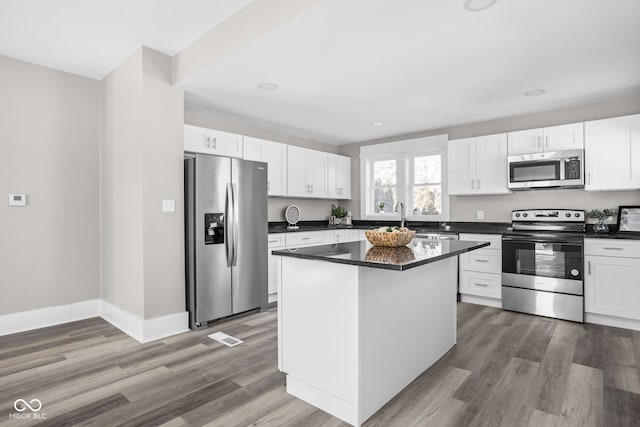 kitchen with sink, dark wood-type flooring, appliances with stainless steel finishes, white cabinets, and a kitchen island