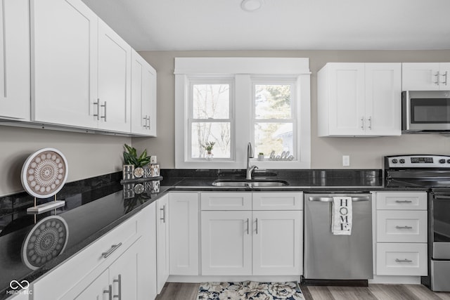 kitchen with appliances with stainless steel finishes, sink, dark stone countertops, and white cabinets