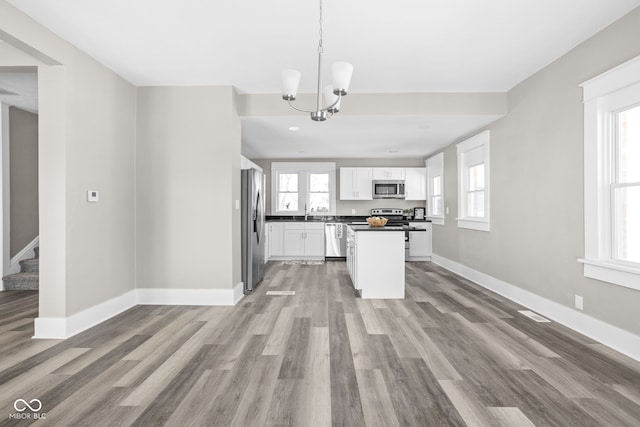 kitchen with plenty of natural light, appliances with stainless steel finishes, hanging light fixtures, and white cabinets