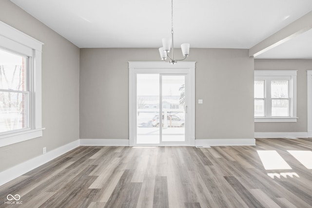 unfurnished dining area featuring a wealth of natural light, light hardwood / wood-style floors, and a notable chandelier