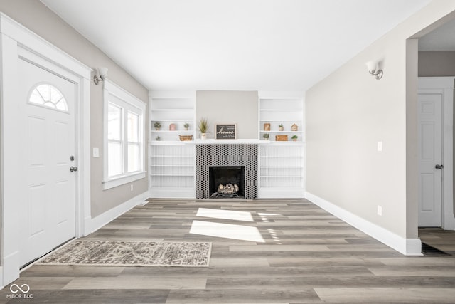 unfurnished living room with a fireplace, built in features, and wood-type flooring