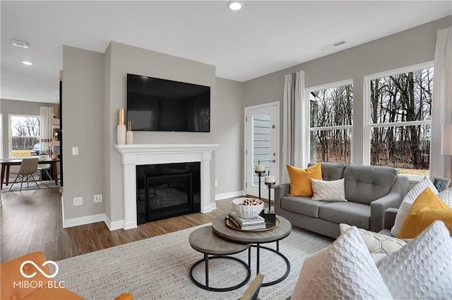 living room featuring recessed lighting, visible vents, a glass covered fireplace, wood finished floors, and baseboards