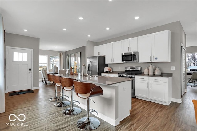 kitchen with stainless steel appliances, a center island with sink, a sink, and white cabinetry