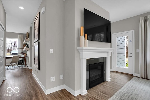 living room featuring a glass covered fireplace, dark wood-style flooring, baseboards, and recessed lighting